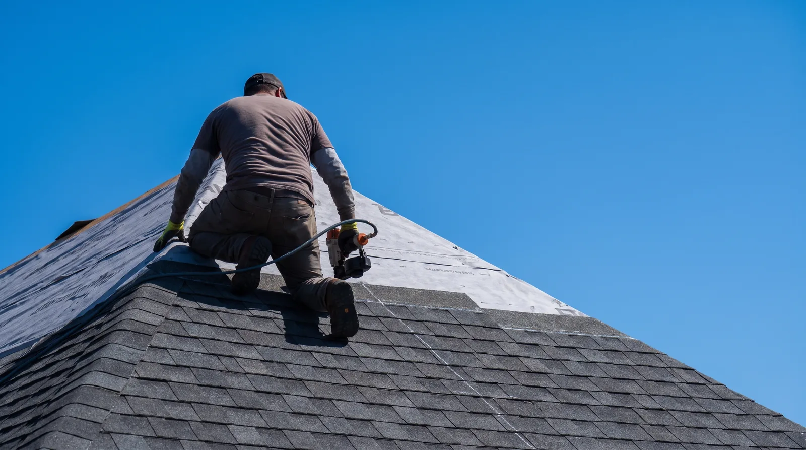 Roofer nailing Class 4 impact-resistant architectural shingles over synthetic underlayment on a steep gable